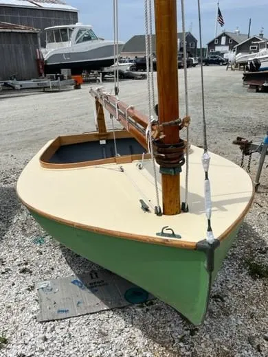 The Image of 1984 Beetle Cat Boat with wooden mast, docked on gravel, surrounded by other boats. - 1
