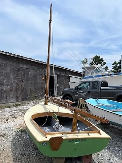 Slide: The Image of 1984 Beetle Cat Boat with green hull, docked near rustic building and truck. - 4