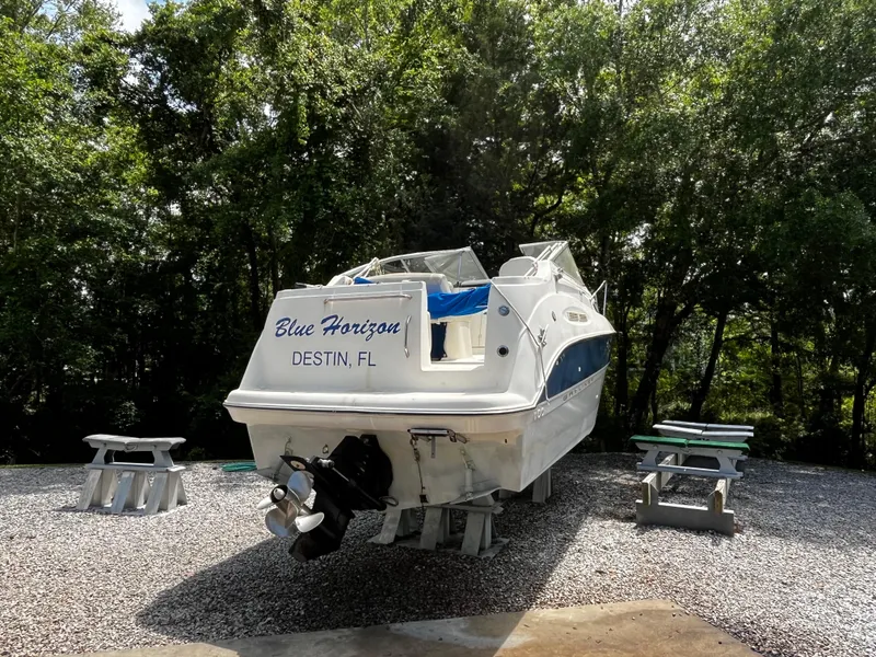 Slide: The Image of 2005 Bayliner 245 boat named "Blue Horizon" in Destin, FL, on gravel with trees. - 3