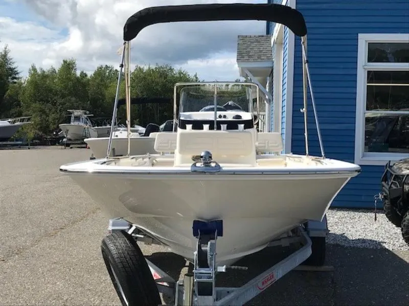 Slide: The Image of 2025 Boston Whaler 170 Montauk boat on trailer, parked near blue building. - 11