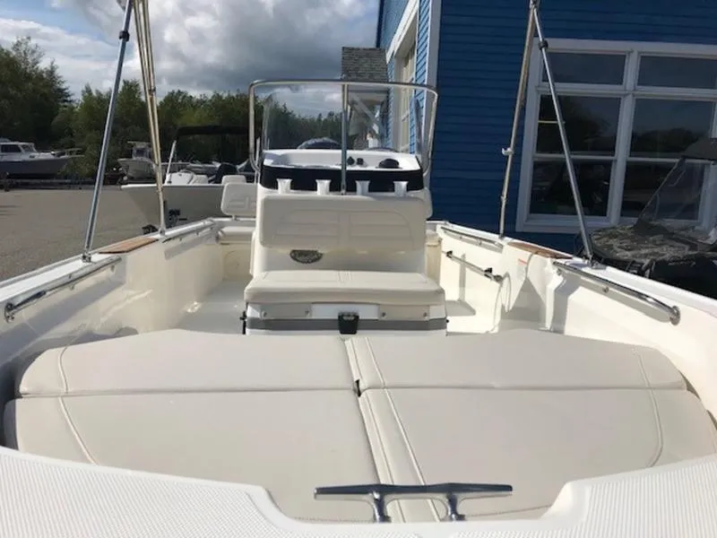 Slide: The Image of 2025 Boston Whaler 170 Montauk boat interior with seating and console, docked near blue building. - 13