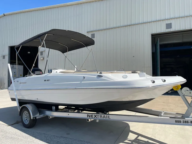 Slide: The Image of 2021 Hurricane SunDeck Sport 201 OB boat on trailer, parked outside a warehouse. - 2