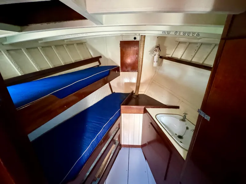 Slide: The Image of 1966 Rampart 48 yacht interior with wooden paneling, blue cushioned bed, and porthole windows. - 14