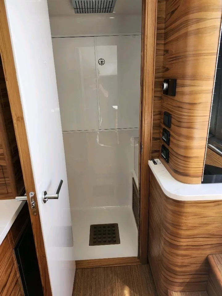 Slide: The Image of 2025 Custom Carolina Mystique M48 boat interior with modern wood finish and shower. - 17
