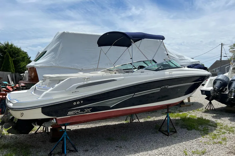 Slide: The Image of 2007 Sea Ray 250 SLX boat on stands, white and black hull, blue bimini top. - 2