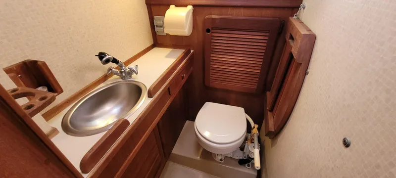 Slide: The Image of 1986 Island Packet 27 Sloop bathroom with sink, toilet, and wooden cabinetry. - 17