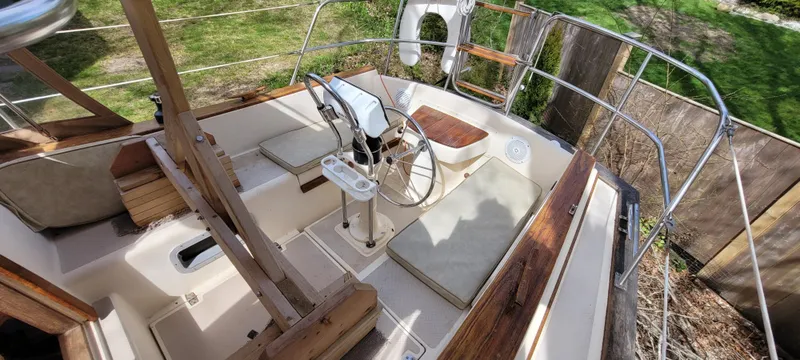 Slide: The Image of 1986 Island Packet 27 Sloop cockpit with steering wheel, seating, and wooden accents. - 25