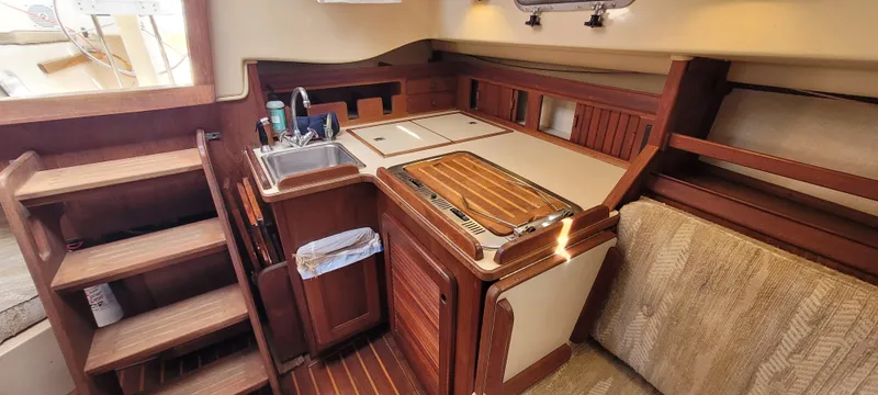 Slide: The Image of 1986 Island Packet 27 Sloop interior with wooden cabinetry and compact kitchen area. - 5