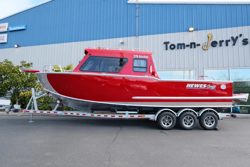 Slide: The Image of 2024 Hewescraft 270 Alaskan boat in vibrant red on a trailer outside dealership. - 2