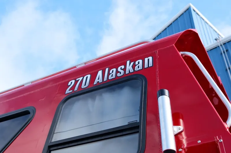 Slide: The Image of Red 2024 Hewescraft 270 Alaskan boat exterior with windows and railing. - 7