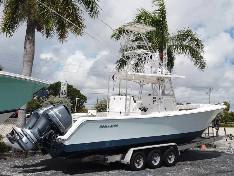 Slide: The Image of 2005 Regulator 32 Forward Seating boat on trailer, parked near palm trees under a cloudy sky. - 31