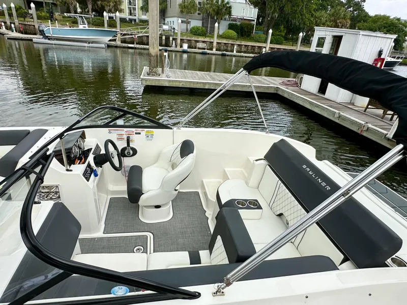 Slide: The Image of 2022 Bayliner DX 2050 boat interior with seating and steering, docked by a calm waterfront. - 4