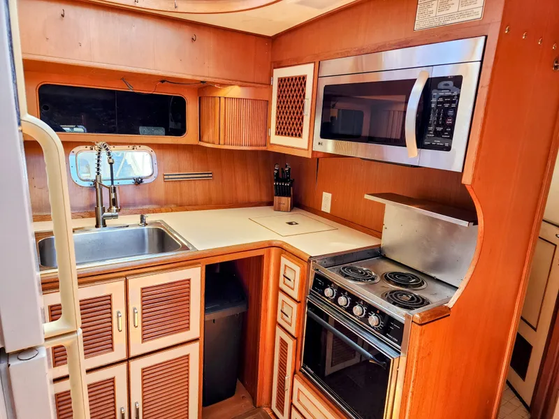 Slide: The Image of 1987 Hi-Star Yacht Fisher 55 kitchen with stove, microwave, sink, and wooden cabinets. - 32