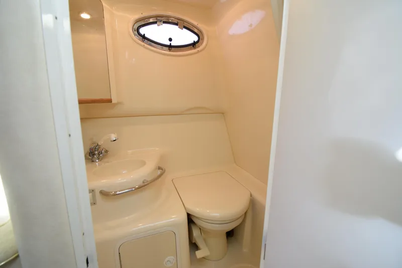 Slide: The Image of 1999 Sea Ray 290 Sundancer bathroom with sink, toilet, and porthole window. - 25