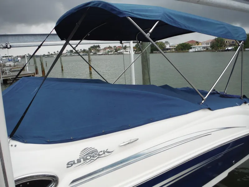 Slide: The Image of 2007 Sea Ray 240 Sundeck boat with blue cover docked by the water. - 31