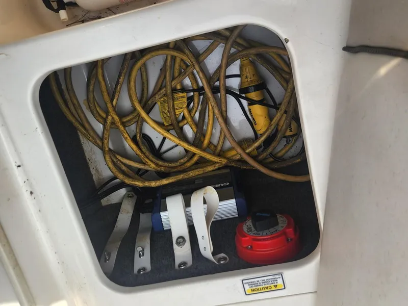 Slide: The Image of 2003 Sea Ray 220 Sundeck storage compartment with electrical cables and battery switch. - 15