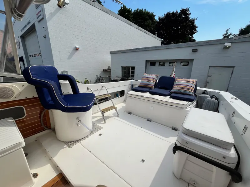 Slide: The Image of 1977 Bertram 26 Moppie boat interior with blue seating and striped cushions, docked near white buildings. - 14