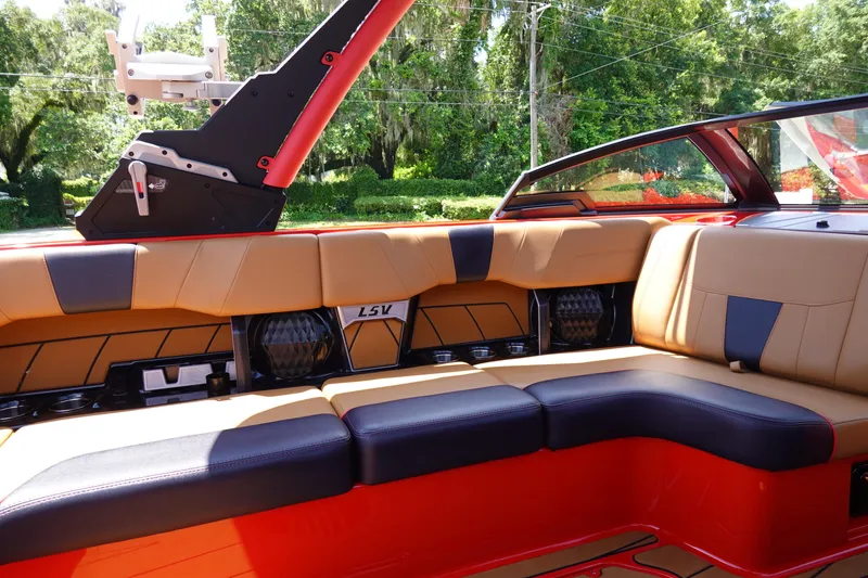Slide: The Image of 2023 Malibu 23 LSV boat interior with tan and black seating, red accents, and lush greenery background. - 14