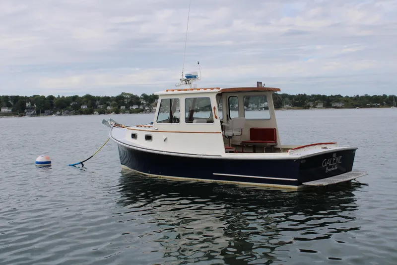 Slide: The Image of 1996 Webbers Cove 26 boat anchored on calm water with scenic shoreline background. - 4