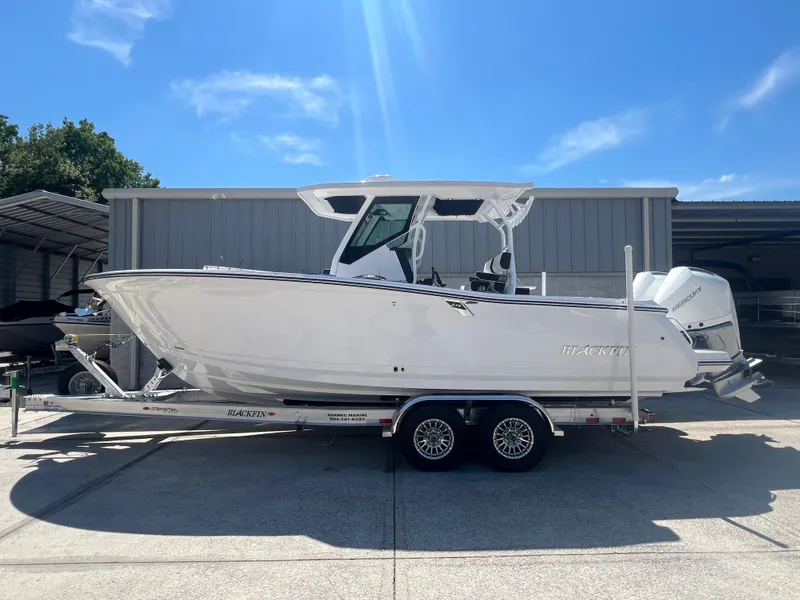 Slide: The Image of 2024 Blackfin 272 CC boat on a trailer, parked outdoors under a clear blue sky. - 1