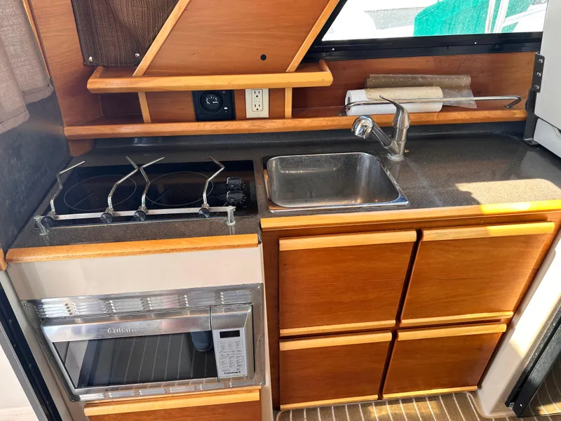 Slide: The Image of 2014 Cutwater C 26 boat kitchen with stove, sink, microwave, and wooden cabinetry. - 18