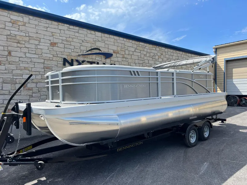 Slide: The Image of 2024 Bennington 22S pontoon boat on trailer, parked outside a building. - 1