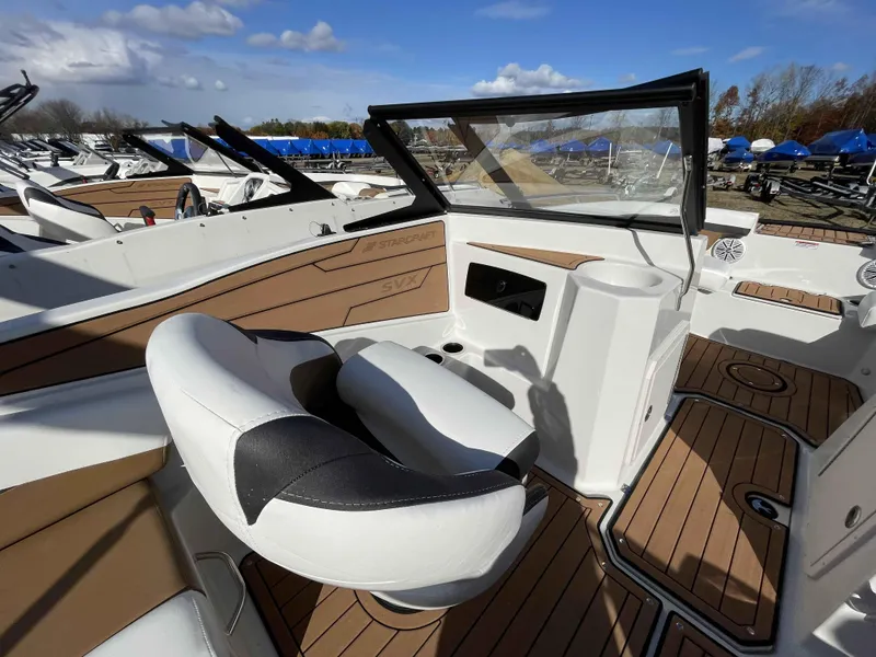 Slide: The Image of 2023 Starcraft SVX 210 OB boat interior with white and tan seating, wood flooring, and open windshield. - 11
