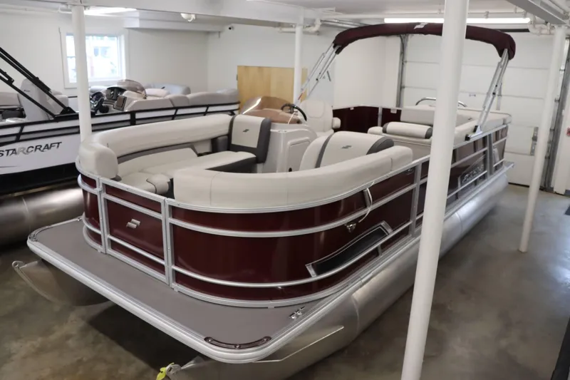 Slide: The Image of 2023 Starcraft EX 22C pontoon boat in showroom, featuring maroon and white seating. - 1