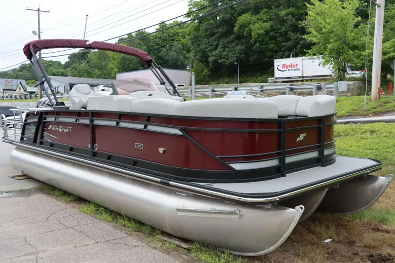 Slide: The Image of 2023 Starcraft CX 23Q DH pontoon boat with maroon exterior, parked on grass. - 2