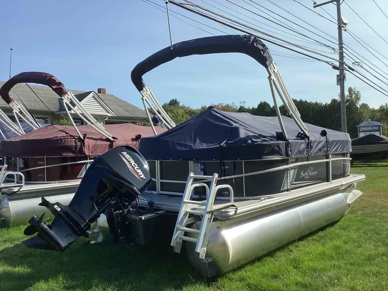 Slide: The Image of 2023 SunChaser VISTA 16LR pontoon boat with Mercury outboard motor, covered and parked on grass. - 3