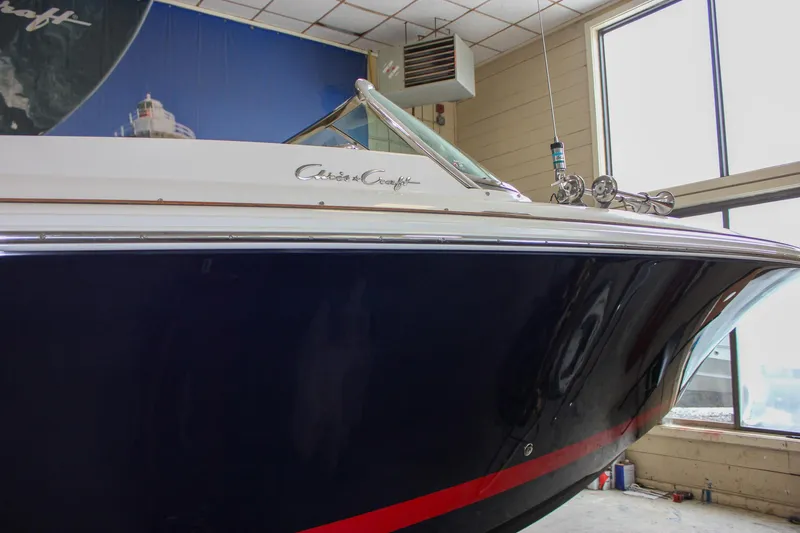 Slide: The Image of 2004 Chris-Craft 28 Launch boat in showroom, featuring sleek navy and white design. - 10