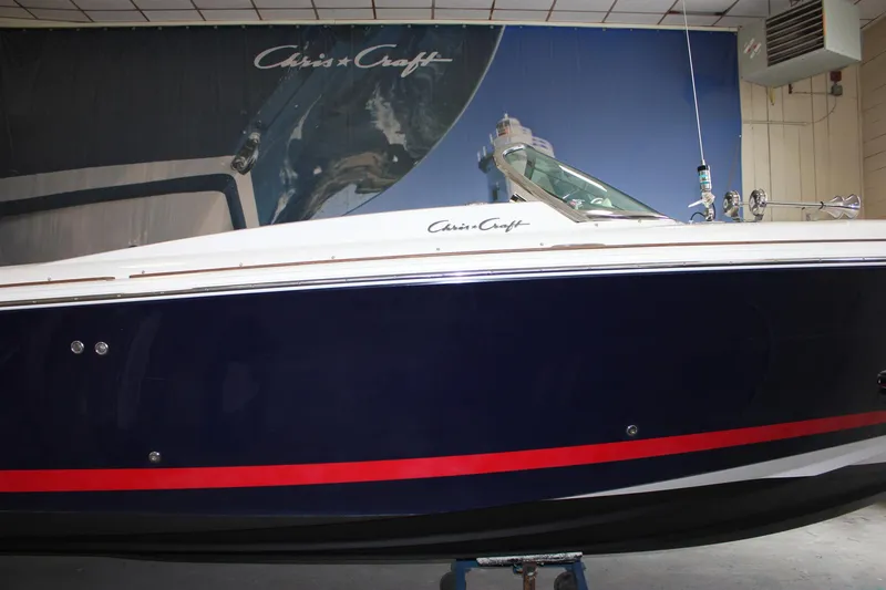 Slide: The Image of 2004 Chris-Craft 28 Launch boat with navy blue hull and red stripe in showroom. - 3