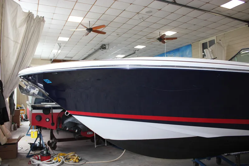 Slide: The Image of 2004 Chris-Craft 28 Launch boat in indoor storage, featuring sleek navy and red design. - 48