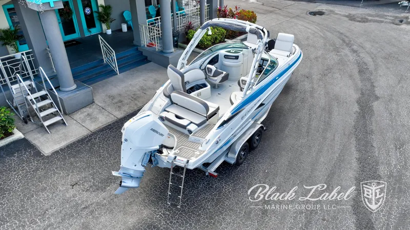 Slide: The Image of 2024 Crownline E260 XS boat, white and blue, parked on a trailer outside a building. - 5