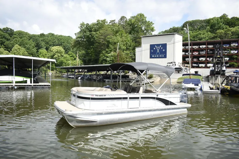 The Image of 2023 Bennington 22 SXCW pontoon boat docked at a marina with lush green trees. - 0
