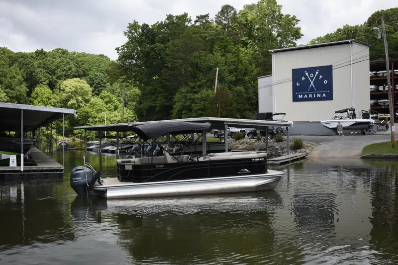 Slide: The Image of 2023 Bennington 23 XSL3 pontoon boat docked at a marina with lush green trees. - 2