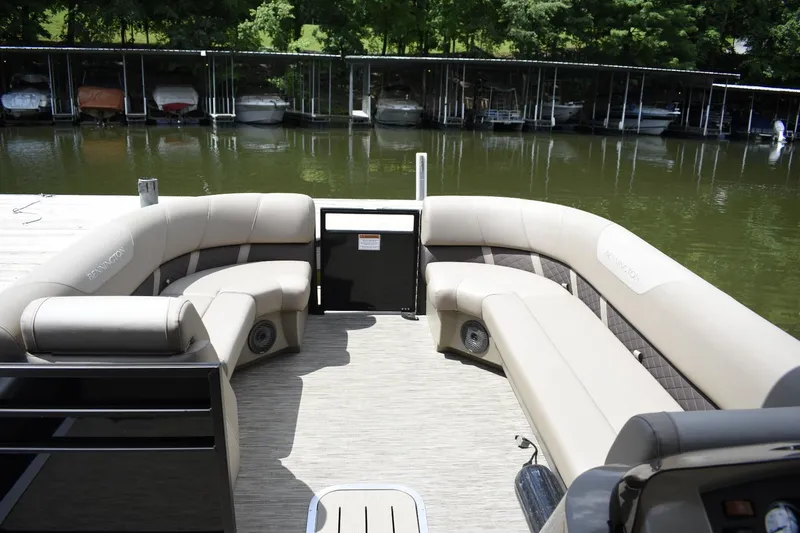 Slide: The Image of 2023 Bennington 23 XSL3 pontoon boat interior with beige seating, docked by the lake. - 4