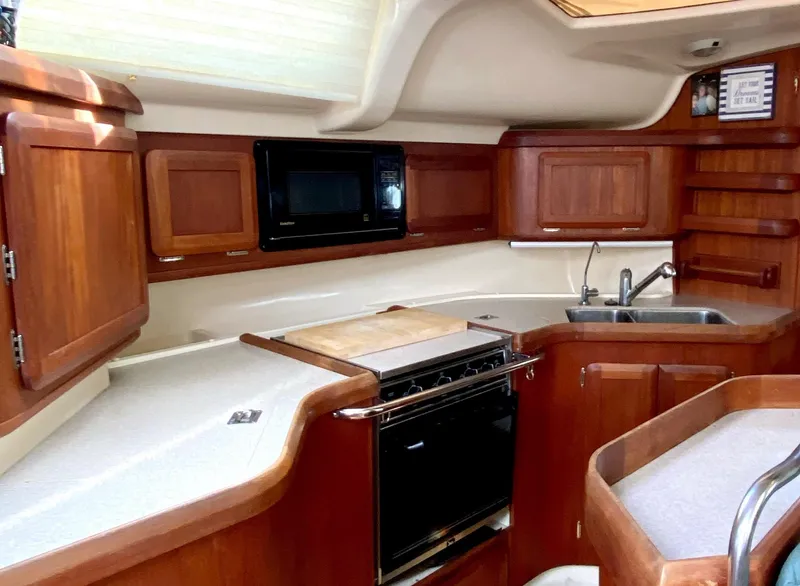 Slide: The Image of Hunter 430 yacht kitchen interior, 1997 model, featuring wooden cabinetry, stove, microwave, and sink. - 14
