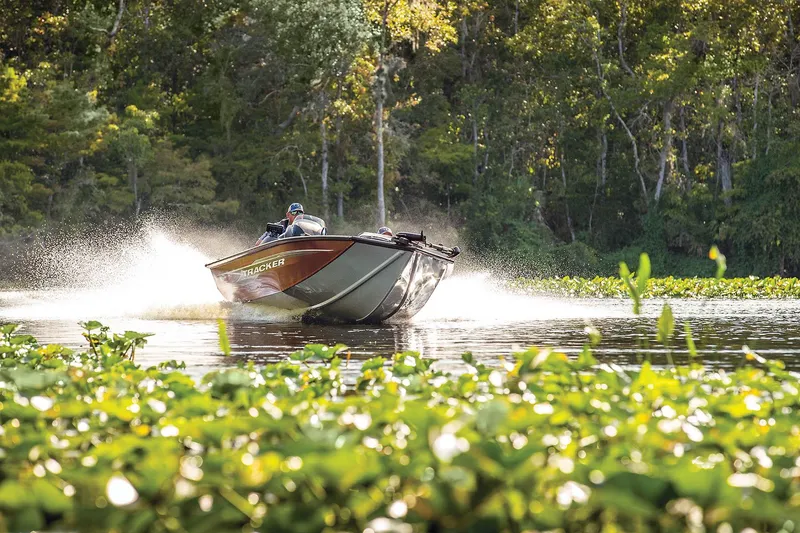 Slide: The Image of 2024 Tracker Pro Team 175 TXW boat speeding on a lake surrounded by greenery. - 5