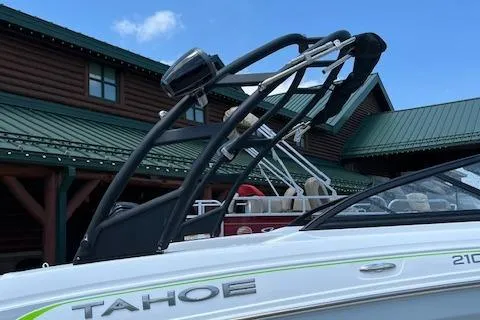 Slide: The Image of 2024 Tahoe 210 S boat with wakeboard tower, docked near a wooden cabin. - 10
