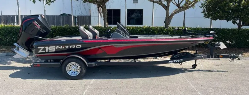 Slide: The Image of 2024 Nitro Z19 fishing boat with trailer, black and red design, parked outdoors. - 12
