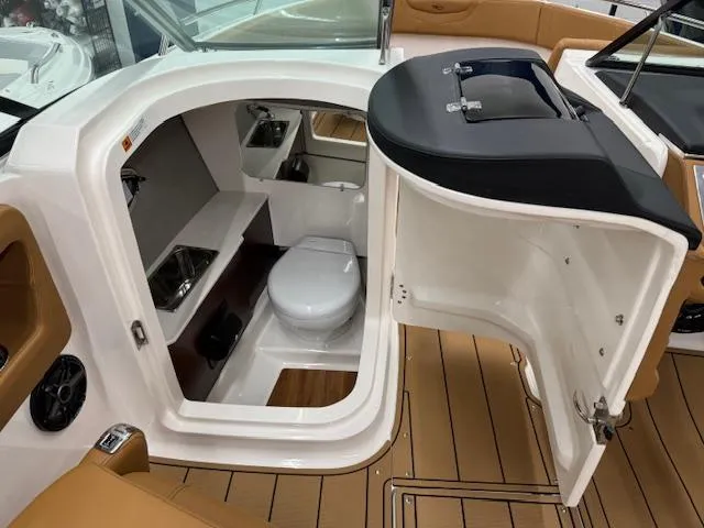 Slide: The Image of 2025 Chaparral 250 OSX boat interior with compact bathroom and wooden flooring. - 11