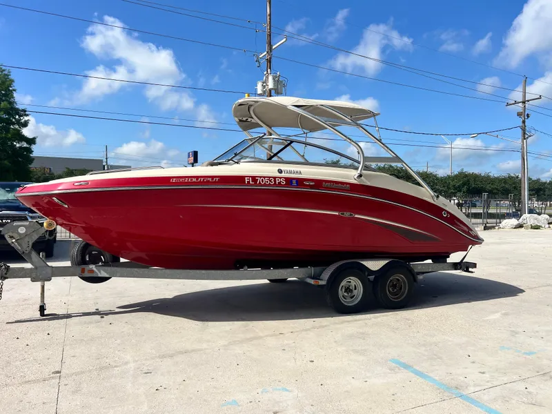 Slide: The Image of 2014 Yamaha Boats 242 Limited S in red on a trailer under blue skies. - 5