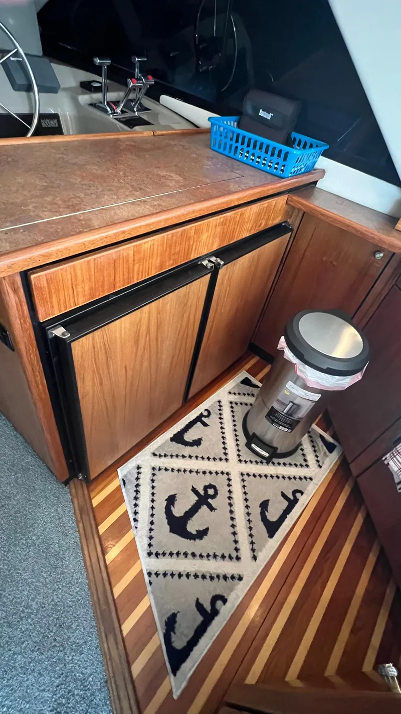 Slide: The Image of 1999 Bayliner 3988 Motoryacht interior with wood cabinetry, anchor-themed rug, and stainless steel trash can. - 13