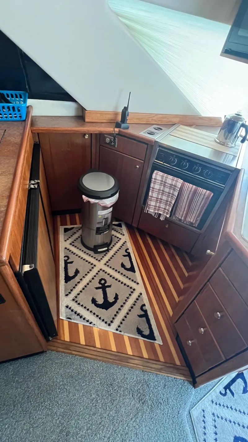 Slide: The Image of Interior of 1999 Bayliner 3988 Motoryacht kitchen with wooden cabinets and nautical-themed rug. - 14
