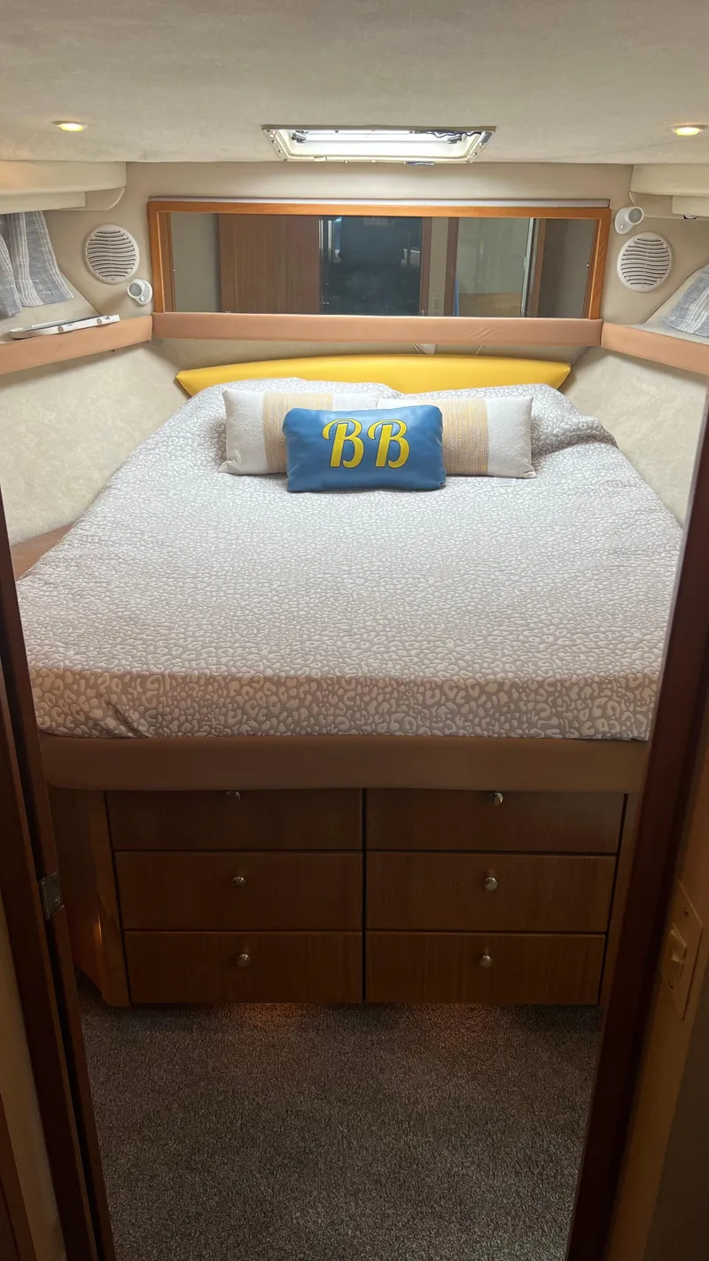 Slide: The Image of 1999 Bayliner 3988 Motoryacht bedroom with cozy bed, decorative pillows, and wooden storage drawers. - 16