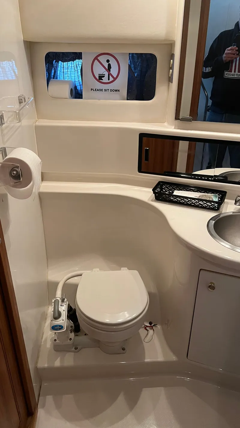 Slide: The Image of 1999 Bayliner 3988 Motoryacht bathroom with toilet, sink, and "Please Sit Down" sign. - 22