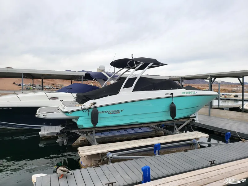 Slide: The Image of 2023 Monterey M22 boat docked at marina, turquoise hull, black canopy, overcast sky. - 16