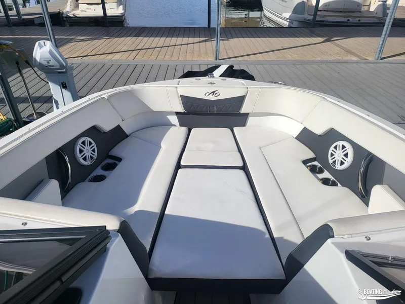 Slide: The Image of 2023 Monterey M22 boat interior with cushioned seating and cup holders at a dock. - 28