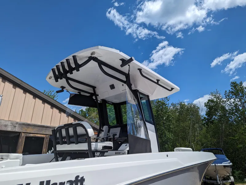 Slide: The Image of 2024 Wellcraft 223 Fisherman boat with T-top and seating, docked under a blue sky. - 3